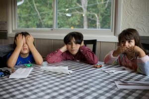 Drei Kinder bedecken ihre Augen an einem Tisch in einem Restaurant.