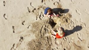 Zwei Kinder spielen im Sand am Strand.