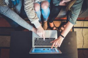 Drei Frauen schauen auf einen Laptop auf einem Couchtisch.