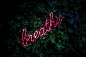 Eine rosafarbene Leuchtreklame mit dem Wort „Breathe“ vor dunklem Hintergrund.