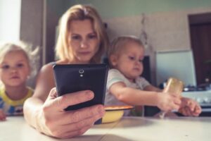 Eine Frau hält ein Mobiltelefon in der Hand, während ihre Kinder darauf schauen.